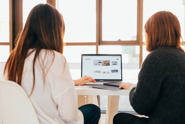 two women talking while looking at laptop